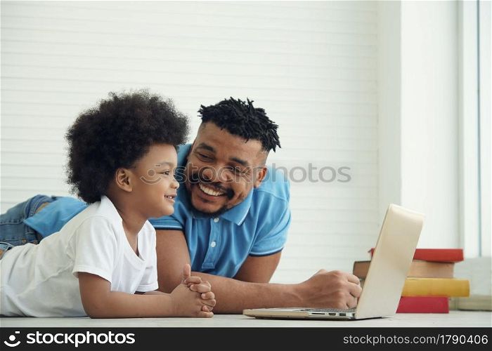 Happy African American family father and little son lying on floor and online learning with laptop at home
