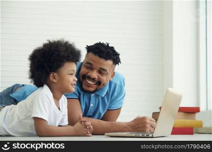 Happy African American family father and little son lying on floor and online learning with laptop at home