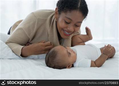 Happy African American family, young mother smiling holding her cute newborn baby girl hand and lying on bed together at bedroom at home. Motherhood, child care concept