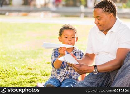 Happy African American Father and Mixed Race Son Playing with Paper Airplanes in the Park.