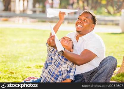 Happy African American Father and Mixed Race Son Playing with Paper Airplanes in the Park.