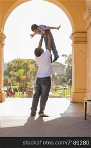 Happy African American Father Lifts Mixed Race Son Over His Head in the Park.