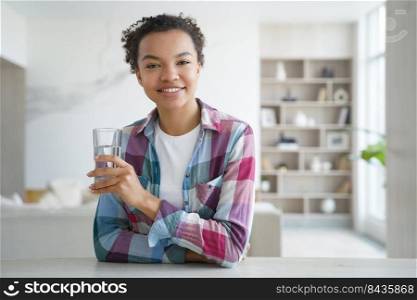 Happy african american girl drinks pure water from a glass. Gorgeous young woman has mineral water at home. Weight loss dieting, refreshing and detox. Healthy lifestyle, morning health routine.. Happy african american girl drinks water from a glass. Healthy lifestyle, morning health routine.