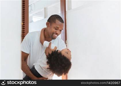 Happy African American hugging with little kid boy on holiday. Black Father and son in white clothes cuddling playing together at home. Toothy smile, Love emotion, Family having fun.