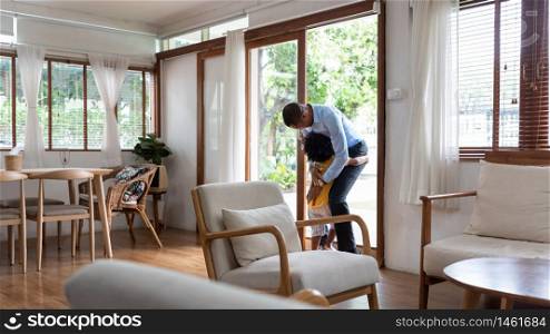 Happy African American little child hugging with Dad together when he arriving at the door. Happy Smiling Black Father in blue shirt is embracing his son in yellow cloth at home. Family Love emotion