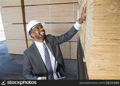 Happy African American male contractor inspecting wooden planks while holding tablet PC