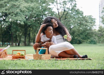 Happy African family Mother and son picnic together at garden green park on weekend. A little boy sitting on his mom s lap. Young mom pat her kid head