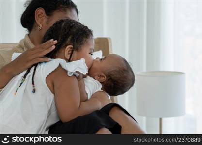 Happy African family, young mother and daughters, little kid older sister tender kissing her newborn baby sister hand while mom looking at children with love and care at bedroom at home