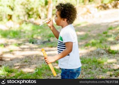 Happy african little boy playing with soap bubbles in nature