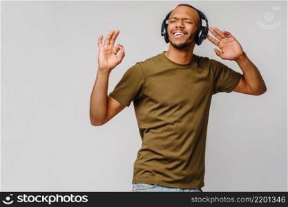 Happy african man smiling listening to music in headphones over grey background.. Happy african man smiling listening to music in headphones over grey background