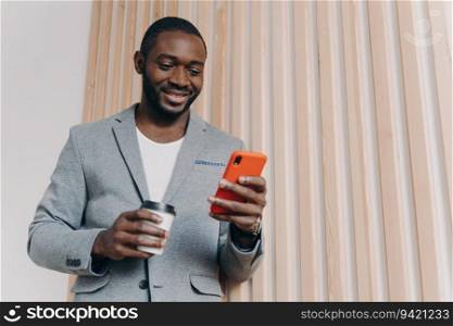 Happy African office worker in suit, coffee break, using mobile phone, chatting with friends, texting/emailing, smiling and looking at smartphone.