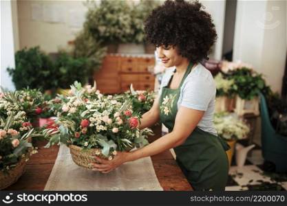 happy african woman arranging basket flowers desk