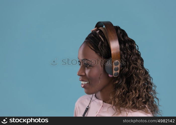 Happy African Woman listening to music on headphones. Young fresh African female model on blue background.