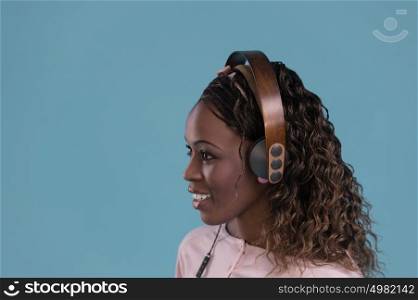 Happy African Woman listening to music on headphones. Young fresh African female model on blue background.