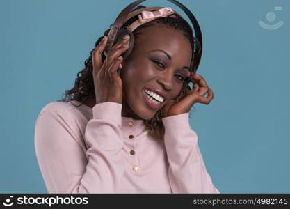 Happy African Woman listening to music on headphones. Young fresh African female model on blue background.