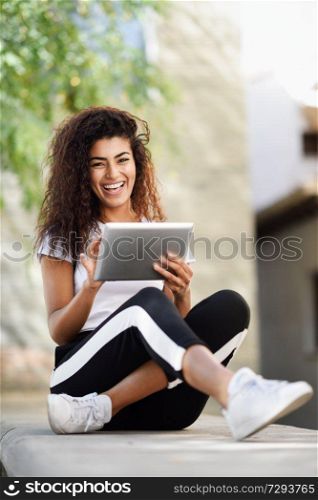 Happy African woman using digital tablet outdoors. Arab girl wearing sportswear and smiling in urban background. Happy African woman using digital tablet outdoors