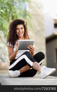 Happy African woman using digital tablet outdoors. Arab girl wearing sportswear and smiling in urban background. Happy African woman using digital tablet outdoors