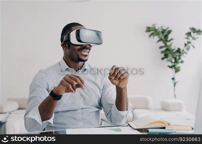 Happy afro guy in vr headset at home. Busi≠ssman has virtual meeting. Freelancer is working on startup design project. Modern∫eractive gad≥t for distant work and entertainment.. Freelancer in vr headset is working on startup project. Modern∫eractive gad≥t for distant work.
