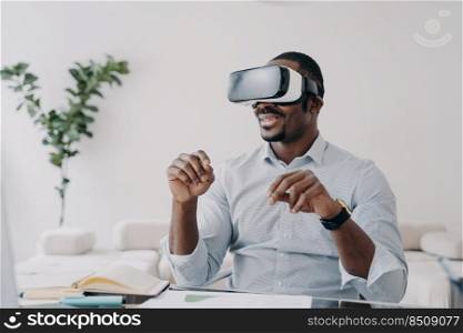 Happy afro guy in vr headset at home. Businessman has virtual meeting. Freelancer is working on startup design project. Modern interactive gadget for distant work and entertainment.. Freelancer in vr headset is working on startup project. Modern interactive gadget for distant work.