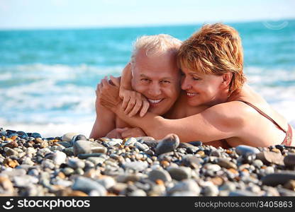 happy aged pair lie on pebble beach, focus on woman