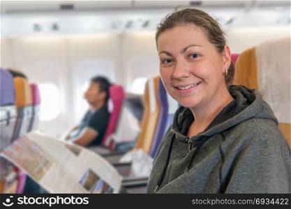 happy airplane passenger with magazine in chair smiling during flight