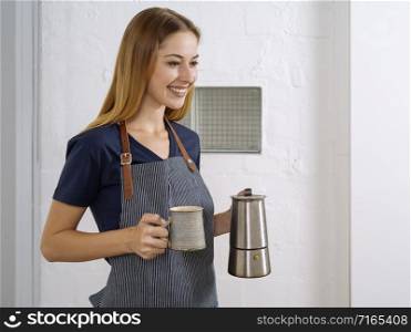 Happy and beautiful young blond woman wearing an apron and serving coffee.