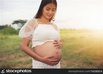 happy and proud pregnant Asian woman looking at her belly in a park at sunrise