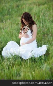 Happy and relaxed pregnant woman sitting on the grass