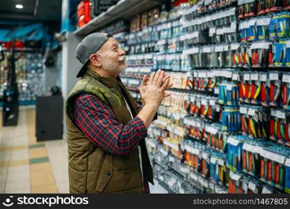 Happy angler choosing hooks and baubles in fishing shop. Equipment and tools for fish catching and hunting, accessory choice on showcase in store, bait assortment. Angler choosing hooks and baubles in fishing shop