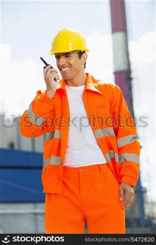 Happy architect wearing reflective workwear communicating on walkie-talkie at site