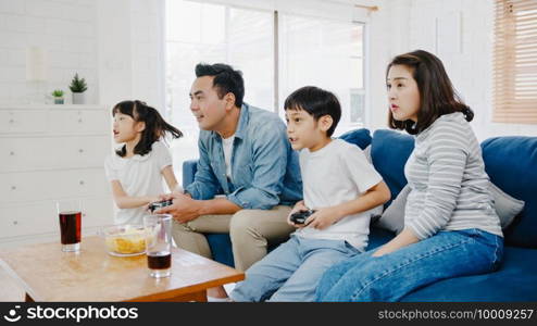 Happy Asia family dad, mom and kids funny playing video game with technology console in living room at house. Self-isolation, stay at home, social distancing, quarantine for coronavirus prevention.