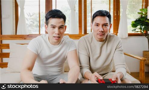 Happy asia young gay couple sit on couch use joystick controller play video game spend fun time together in living room at house. Married couple family lifestyle, LGBTQ Couple stay at home concept.