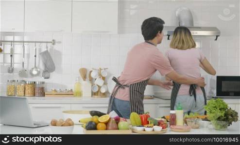 Happy Asian beautiful family couple husband and wife cooking vegetable salad in kitchen together at home. The man sneaked in to pretend to tickle the waist woman. healthy food concept