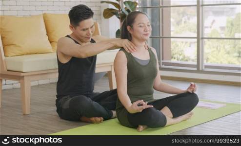 Happy Asian beautiful lifestyle family couple, woman doing YOGA sitting meditating on lotus pose workout at home and the man massage shoulder for relax. sport healthy concept