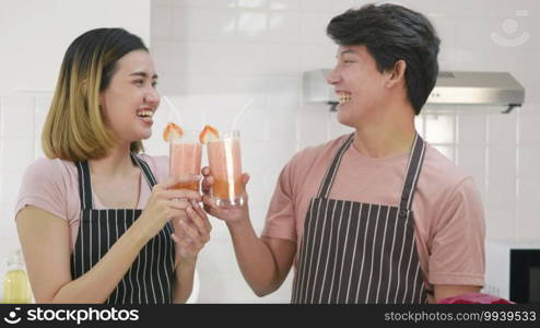 Happy Asian beautiful young family couple husband and wife enjoying drinking fresh apple smoothie juice in kitchen on glass together in morning at home. Healthy lifestyle concept,