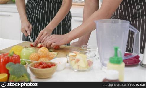 Happy Asian beautiful young family couple husband and wife making fresh smoothie in kitchen together at home. The man and woman slicing fresh apple fruits and veggies. Healthy lifestyle concept