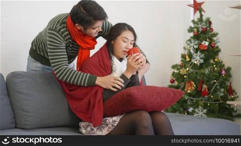 Happy Asian beautiful young family couple husband and wife on sofa in home living room, Loving man covering blanket to woman sit on sofa drink tea showing care warming, winter holidays concept