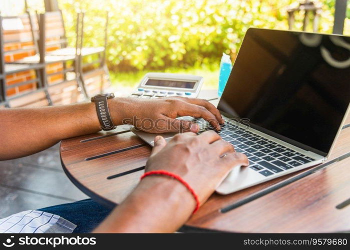 Happy Asian black businessman person or office worker wear face mask protect sitting on desk work from home using laptop computer typing keyboard and connect networking online at the coffee cafe shop