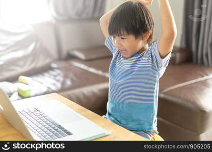 Happy asian boy in blue shirt using computer on wooden desk at home .Asian child smiling and happiness playing computer at room.