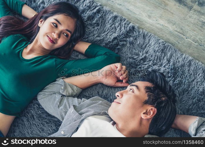 Happy Asian couple lying together on carpet at living room floor. Love relationship and lifestyle concept.