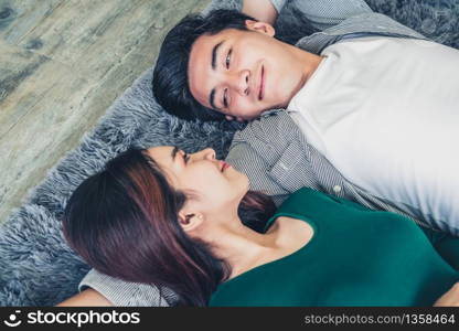 Happy Asian couple lying together on carpet at living room floor. Love relationship and lifestyle concept.