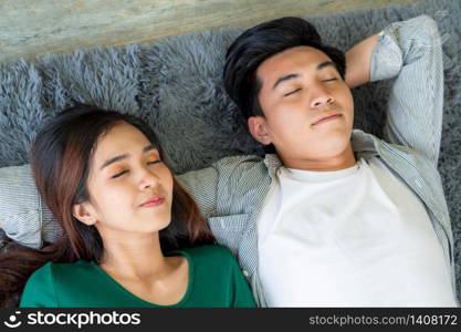 Happy Asian couple lying together on carpet at living room floor. Love relationship and lifestyle concept.