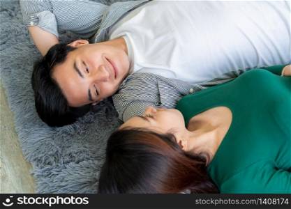 Happy Asian couple lying together on carpet at living room floor. Love relationship and lifestyle concept.