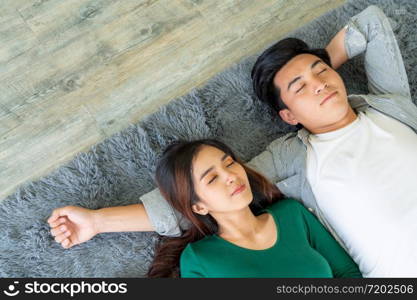 Happy Asian couple lying together on carpet at living room floor. Love relationship and lifestyle concept.