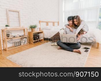 Happy Asian Couple planning and booking the hotel for travel with technology laptop on the bed of bedroom at the modern home, Life style and traveler concept,