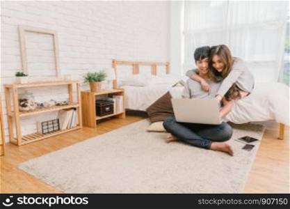 Happy Asian Couple planning and booking the hotel for travel with technology laptop on the bed of bedroom at the modern home, Life style and traveler concept,