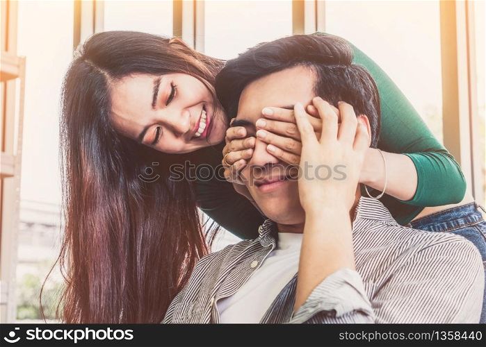 Happy Asian couple play covering eyes in living room.