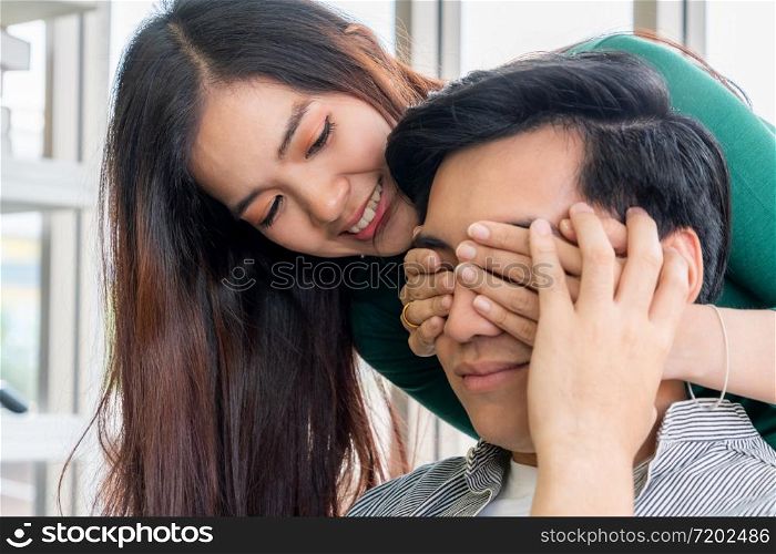 Happy Asian couple play covering eyes in living room.