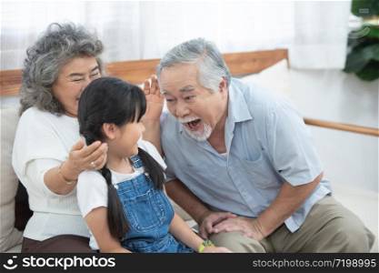 Happy asian elder happy grandfather head touch granddaughter head while sit on sofa and have leisure time together at home.