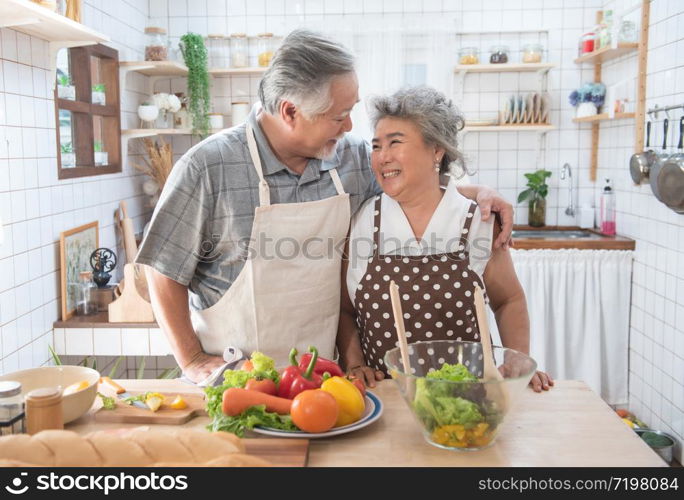 Happy asian elder senior couple cooking fresh meal in kitchen at home.